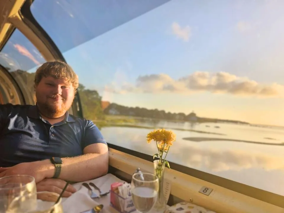 Photo of Kelson Burke sitting in front of a scenic background.
